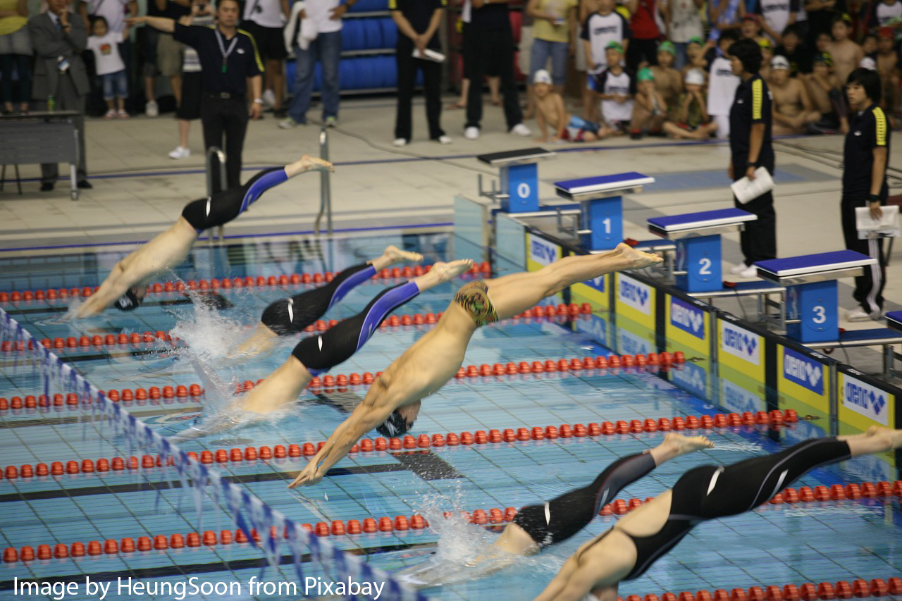 A woman with a yellow cap and black goggles, swimming frontcrawl alongside a blue lane rope