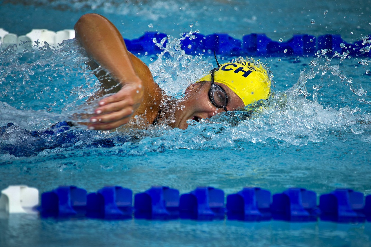 A woman with a yellow cap and black goggles, swimming frontcrawl alongside a blue lane rope
